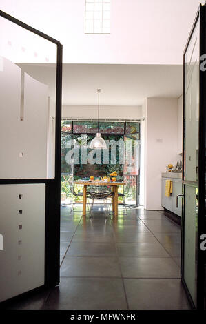 Moderna cucina abitabile con pavimento in piastrelle e aprire le porte in vetro e un tavolo da pranzo in legno e sedie. Foto Stock