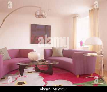 Luminoso soggiorno con rosa e viola divani curvo, arching lampada da terra e grafica tappeto floreale. Foto Stock