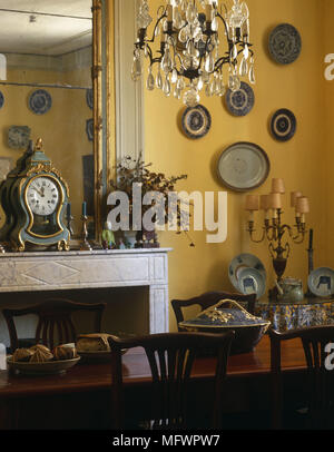 Sala da pranzo con un lampadario sospeso al di sopra di un tavolo di legno davanti al camino con un grande specchio e orologio carrello Foto Stock