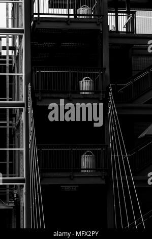 Garage esterno multilivello con primo piano di scale in metallo con ringhiere evidenziate e bidoni per rifiuti. Foto Stock