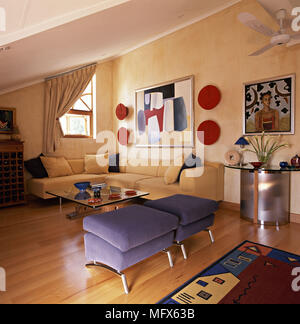 Seduta contemporanea sala con soffitto inclinato divano componibile footstools blu e la parete art. Foto Stock
