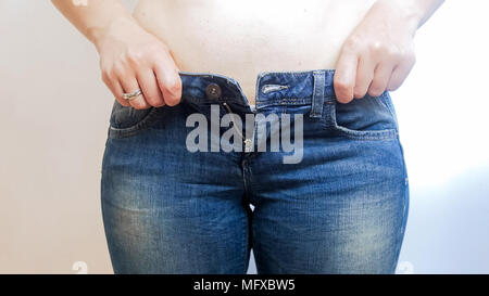 Primo piano della giovane donna sovrappeso lottando indossare jeans stretti Foto Stock