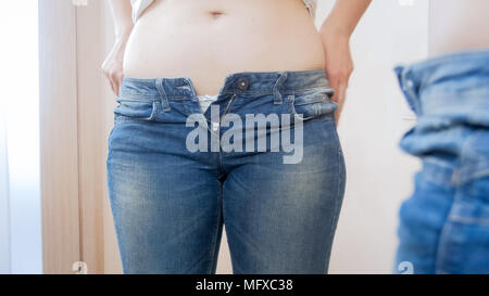 Giovane donna cercando su piccole jeans nella parte anteriore dello specchio Foto Stock