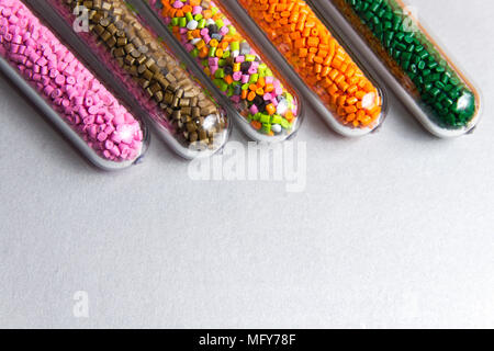 Palline di plastica .del colorante polimerico in tubi di prova su sfondo grigio. Granuli di plastica dopo la trasformazione di rifiuti di polietilene e polipropilene. Foto Stock