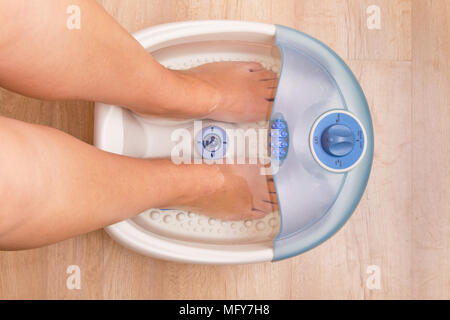 I piedi femminili in un piede vibrante massaggiatore. Massaggio elettrico piede bagno. Pedicure e cura dei piedi. La vista dall'alto Foto Stock