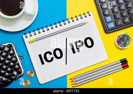 Un notebook con note di Business iniziale offerta di moneta ICO vs IPO Offerta pubblica iniziale con gli strumenti di office giallo su sfondo blu. Concetto di ch Foto Stock