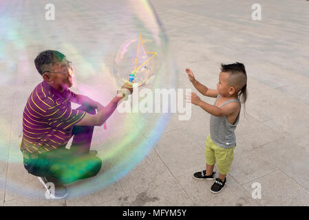 Nonno crea bolle giganti per la nipote durante la riproduzione in city square, Xilinhot, Mongolia Interna, Cina Foto Stock