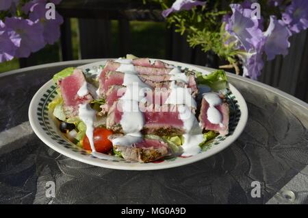 Disseccata Ahi le fette di tonno su un fresco giardino insalata servita al fresco patio tavolo con fiori su un soleggiato serata estiva Foto Stock
