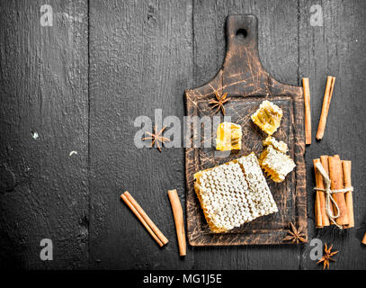 Il miele fresco nei favi e bastoncini di cannella. Su tavoli in legno nero. Foto Stock