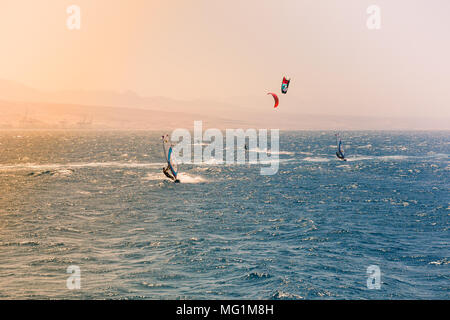 Gli appassionati di windsurf vela in Mar Rosso. Vicino alla spiaggia di Eilat, Israele. Arancio brillante luce proveniente dal sole sulla sinistra. Foto Stock