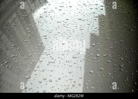 Close-up le gocce di pioggia sul cofano per auto con la riflessione di edifici. Foto Stock