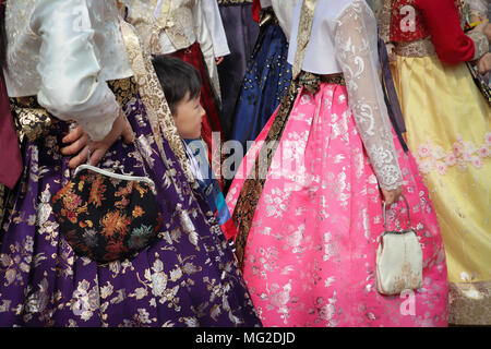 Un ragazzino si nasconde tra le gonne completo in un gruppo di donne coreane che indossano il tradizionale hanbok moda, in colori brillanti. Viste le spalle verso il basso. Foto Stock