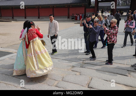 Un gruppo di turisti rush oltre a fotografare due giovani donne abbigliate con vestiti tradizionali Colorati luminosamente hanboks coreano che pongono a Seul, in Corea. Foto Stock