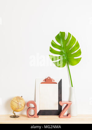 Home moderno decor. Foglio di carta bianco con copia spazio su un clipboard, foglia verde, Globe e lettere di metallo su un ripiano di legno. Foto Stock