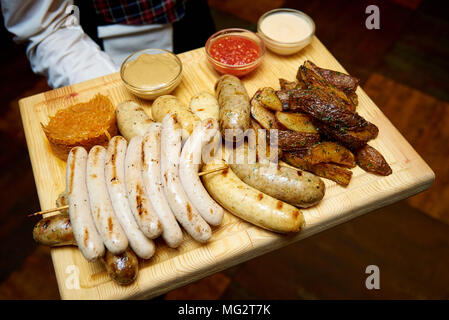 Antipasto per la birra da salsicce e patate con differenti salse su una scheda nelle mani di un cameriere Foto Stock