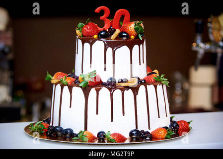 Due-tiered white torta con frutta fresca e cioccolato decorato con una figura di trenta close-up Foto Stock