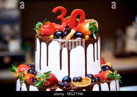 Due-tiered white torta con frutta fresca e cioccolato decorato con una figura di trenta close-up. Foto Stock