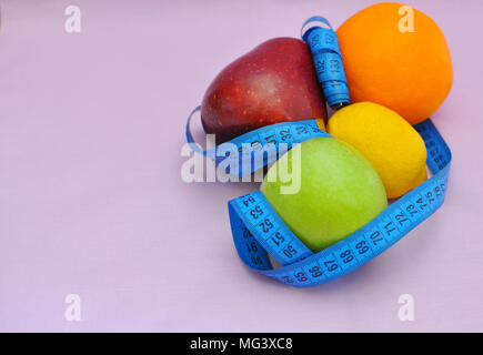 Mele, succo di limone e arancio avvolto con una sartoria blu metro su sfondo rosa, vista laterale superiore, primo piano Foto Stock