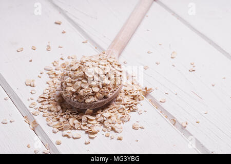 Ammucchiò fiocchi d'Avena Avena Fiocchi di avena sul cucchiaio di legno sul bianco rustico tavolo in legno Foto Stock