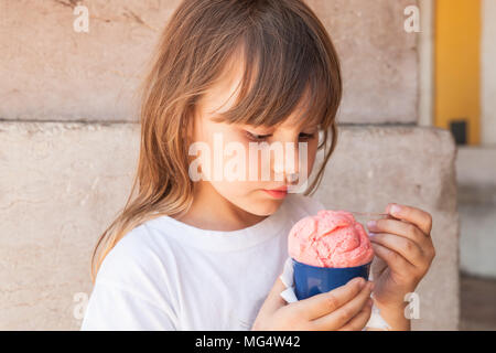 Poco bionda ragazza europea mangia frutta rosa gelato, close up ritratto all'aperto Foto Stock