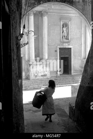 Una giovane donna italiana porta un cesto attraverso le deserte le strade di Roma, Italia negli anni trenta del novecento, eventualmente sul suo modo di mercato. Foto Stock