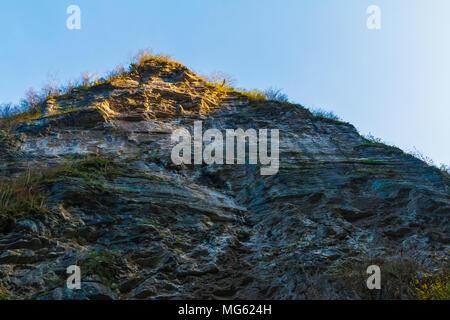 A basso angolo di visione di un alto ripida montagna rocciosa con scogliera illuminata dal sole Foto Stock
