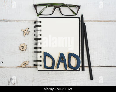 Nota vuota pad per il padre nel porgere le mie congratulazioni, una parola dalle lettere papà, occhiali, una matita, una penna su un bellissimo tavolo bianco. Vista dall'alto di un close-up. Pr Foto Stock