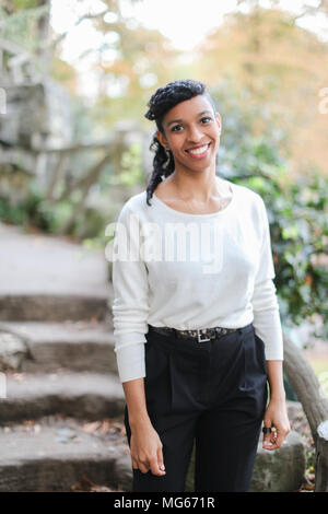 Nero ragazza sorridente indossando camicia bianca e pantaloni in scale di pietra dello sfondo. Concetto di eleganza Afro American persona e bellezza naturale. Foto Stock