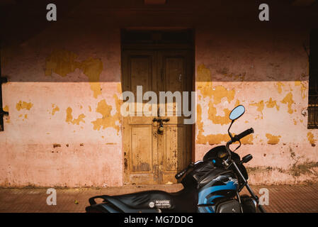 Uno scooter parcheggiato di fronte a un muro di adobe e porta in legno in Goa, India Foto Stock