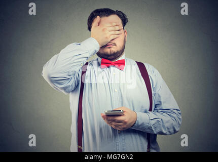 Triste spiacevoli giovane con il telefono cellulare che copre con la mano il suo volto Foto Stock