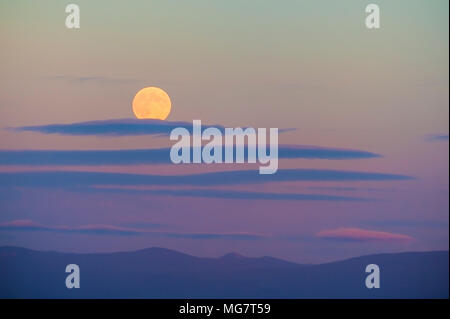 Harvest Moon sopra la Cascade Mountain Range. Il sole di setting aggiunge colori pastello per il cielo mentre le nuvole wispy deriva da. Foto Stock