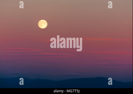 Harvest Moon sopra la Cascade Mountain Range. Il sole di setting aggiunge colori pastello per il cielo mentre le nuvole wispy deriva da. Foto Stock