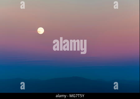 Harvest Moon sopra la Cascade Mountain Range. Il sole di setting aggiunge colori pastello per il cielo mentre le nuvole wispy deriva da. Foto Stock