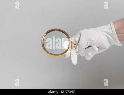 Gli uomini la mano nel guanto bianco azienda golden lente di ingrandimento su bianco Foto Stock