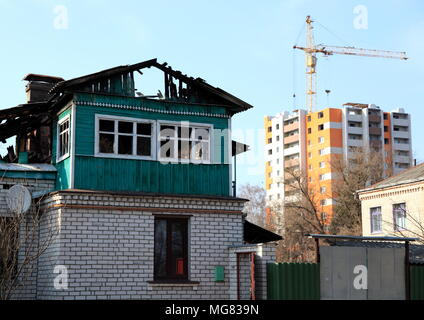 Vecchia casa bruciata sullo sfondo di un nuovo edificio alto in costruzione. Foto Stock