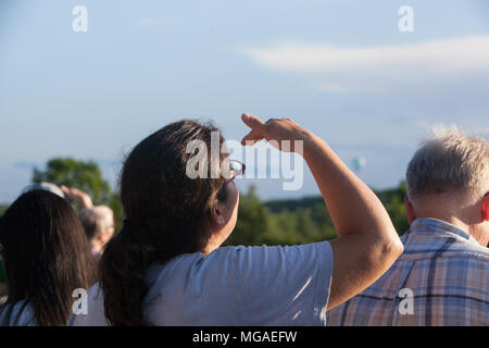 Donna schermare gli occhi dalla luce come alza lo sguardo verso il cielo Foto Stock