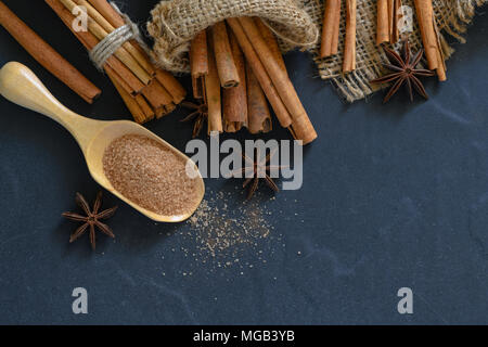 Cannella in polvere mescolare lo zucchero su legno scoop e bastoncini di cannella con anice stellato spice sul blocco di legno, le spezie e le erbe concept Foto Stock