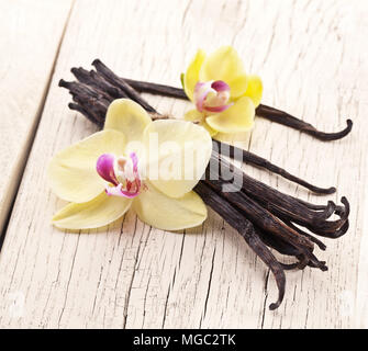 Essiccato baccelli di vaniglia e orchidee vaniglia fiori su sfondo di legno. Foto Stock