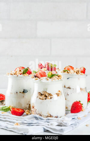 Una sana prima colazione estate idea, casalinghe parfe stratificata dessert in vaso piccolo con muesli, yogurt e fragola, sfondo scuro spazio copia Foto Stock
