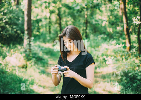 I Capelli rossi ragazza caucasica donna giovane fotografo fotografare il vecchio Retro Vintage fotocamera a pellicola in estate foresta verde. Ragazza vestita di un Nero T Foto Stock