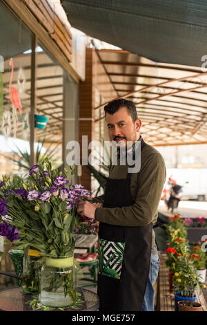 Small business concetto. Fioraio maschio vestita di nero grembiule picking lisianthus fiori dal vaso. Foto Stock