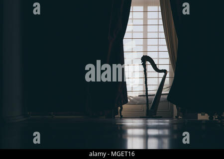 La silhouette di un arpa in un salone di fronte a una porta con tende bianche creano uno spettacolare gioco di luce che può sorprendere Foto Stock