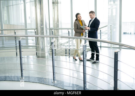 Allegro sorridente elegante razza mista donna manager guardando lo schermo tablet mentre si lavora con un collega come team nel corridoio di office Foto Stock
