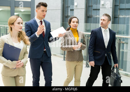 Grave maschio fiducioso manager che lavora con la delegazione e parlare loro di società mentre si cammina su corridoio di office Foto Stock