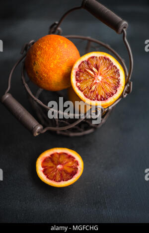 Vintage cesto pieno di organico rosso sanguinosa le arance in legno scuro con tavolo spazio di copia Foto Stock