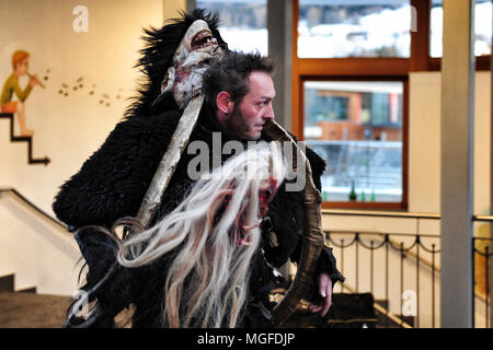 Un uomo che indossa la sua maschera Krampus oltre le sue spalle prima di prendere parte al tradizionale corteo nella città di Castelrotto, Alto Adige. Italia Foto Stock