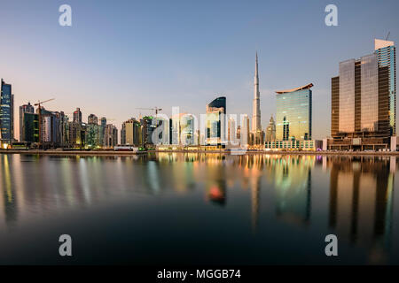 Lo skyline del centro di Dubai, compreso l'iconico Burj Khalifa, si riflette splendidamente sul canale d'acqua prima del tramonto, mostrando la grandezza della città Foto Stock