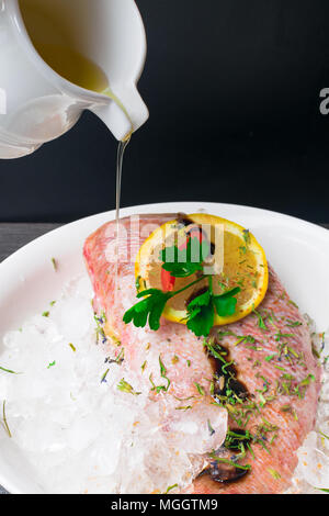 Tutto materie organiche di mare Pesce persico su ghiaccio a cubetti con succo di limone, salsa sy, verdi, pepe rosso, nella piastra bianca su un tavolo scuro dello sfondo. Vista da sopra con copia Foto Stock
