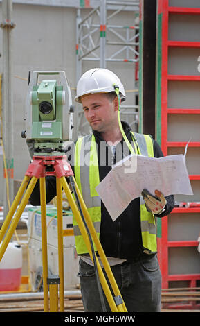 Una costruzione geometra aggiusta un livello elettronico su un grande Londra sito in costruzione. Mostra in acciaio maglia di rinforzo in background. Foto Stock