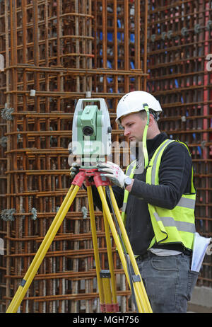 Una costruzione geometra aggiusta un livello elettronico su un grande Londra sito in costruzione. Mostra in acciaio maglia di rinforzo in background. Foto Stock